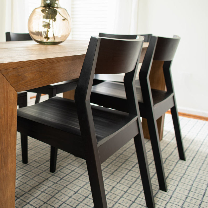 Modern dining room with wooden table and black chairs on patterned rug.