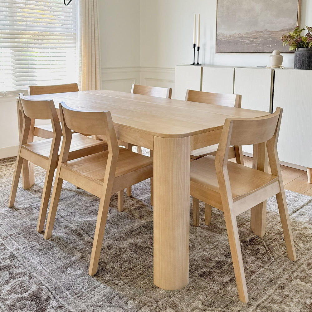 Modern light wood dining table set with six chairs in a bright dining room with natural light.