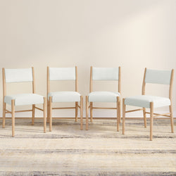 Set of four Scandinavian-style white upholstered dining chairs with light oak frames on neutral rug and beige wall