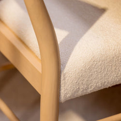 Close-up of modern Scandinavian wooden chair with curved light-wood armrest and beige boucle upholstered seat, textured dining chair detail