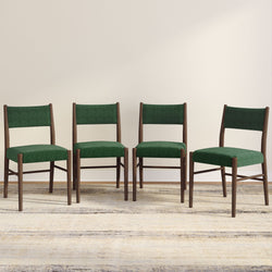 Set of four modern green upholstered dining chairs with wooden frames placed on a neutral rug.