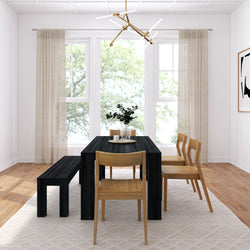 Modern minimalist dining room with black rectangular table, wooden chairs and bench, geometric pendant light, sheer curtains, large sunlit windows and hardwood floor