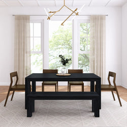 Minimalist modern dining room with black wood table and bench, mid-century wooden chairs, large windows with sheer beige curtains, geometric area rug, and brass linear chandelier