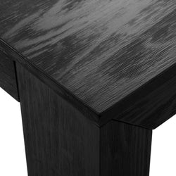 Close-up of black wood dining table corner showing textured wood grain and modern square leg, matte finish