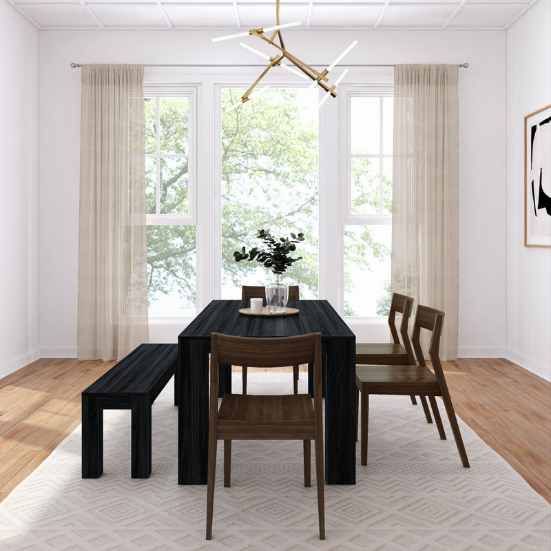Sunlit modern dining room with black wood dining table, bench and wooden chairs, large windows with sheer beige curtains, hardwood floors, modern chandelier and vase of greenery