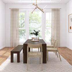 Minimalist dining room featuring a dark wooden table, matching bench, modern chandelier, and light-colored chairs with natural light streaming through large windows.