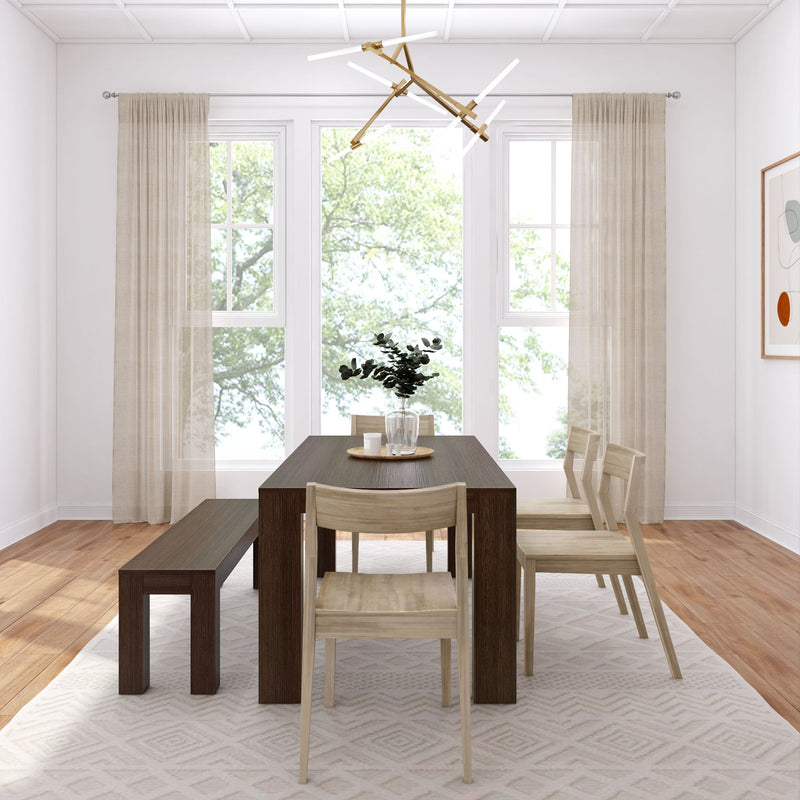 Minimalist dining room featuring a dark wooden table, matching bench, modern chandelier, and light-colored chairs with natural light streaming through large windows.