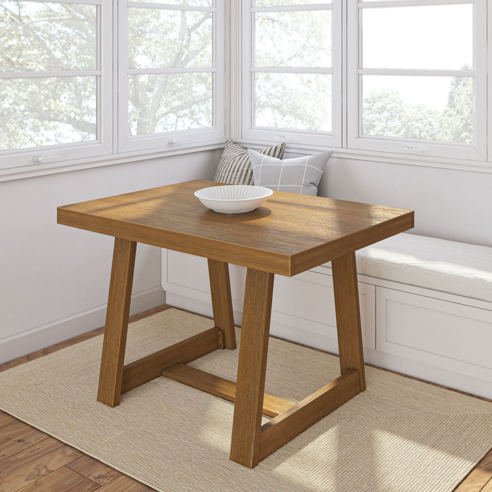 Wooden dining table with a modern design in a bright, sunny breakfast nook with bench seating.