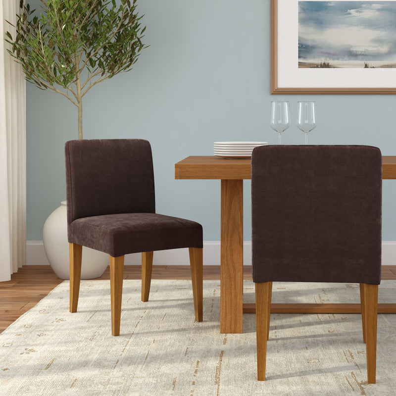 Modern dining room with dark brown upholstered chairs with wooden legs around a rectangular oak dining table, light blue accent wall, potted olive tree, neutral area rug, stacked white plates and wine glasses