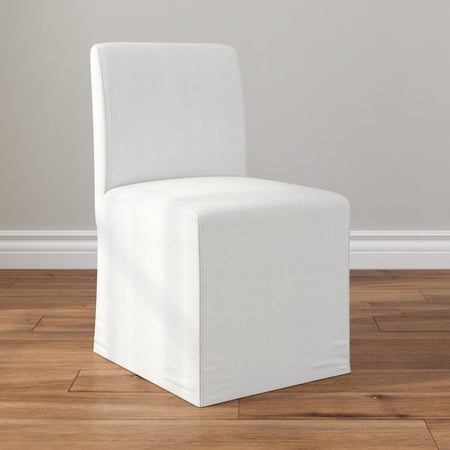 Modern white slipcovered parson dining chair with floor-length skirt on hardwood floor against neutral wall