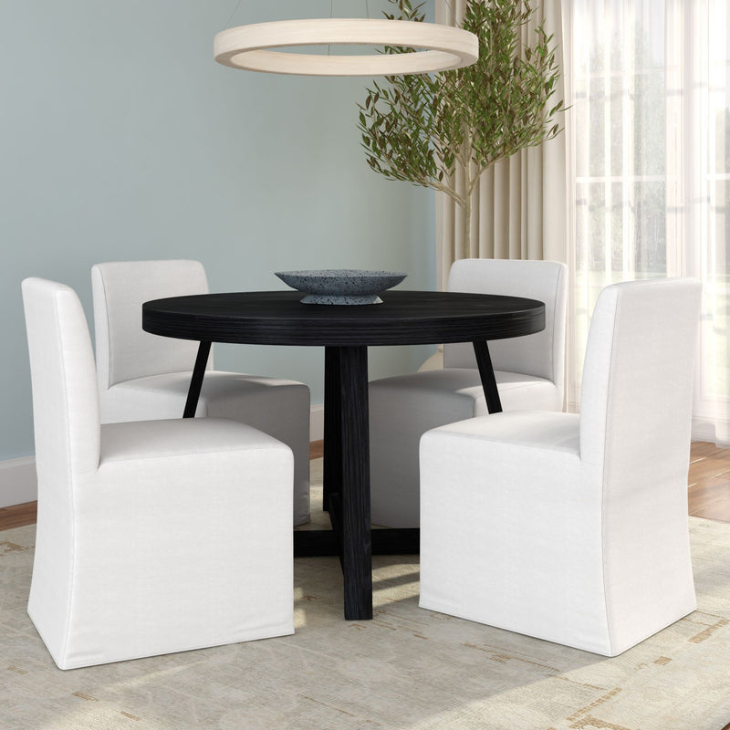 Modern black round dining table with four white slipcovered chairs, circular pendant light, potted olive tree and sheer curtains in bright contemporary dining room