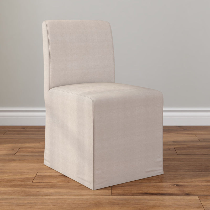 Beige slipcovered upholstered armless Parsons dining chair with linen-look fabric on hardwood floor