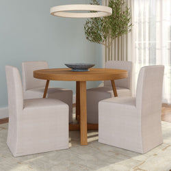 Round oak dining table with four beige slipcovered chairs in a light contemporary dining room featuring a circular pendant light and potted olive tree