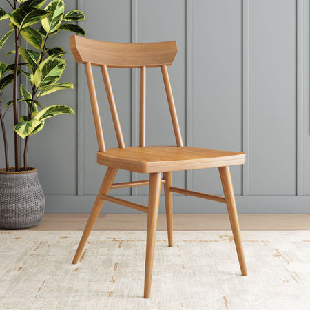 Mid-century modern wooden dining chair in natural oak finish beside a variegated ficus plant against a gray paneled wall in a Scandinavian minimalist interior
