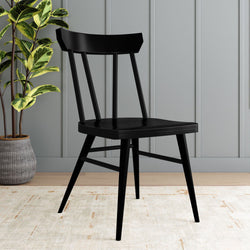 Modern black wooden chair with sleek design against a gray paneled wall, next to a potted green plant on a light textured rug.