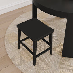 Black wooden stool next to a round black dining table on a beige textured rug over light hardwood floor, modern minimalist seating