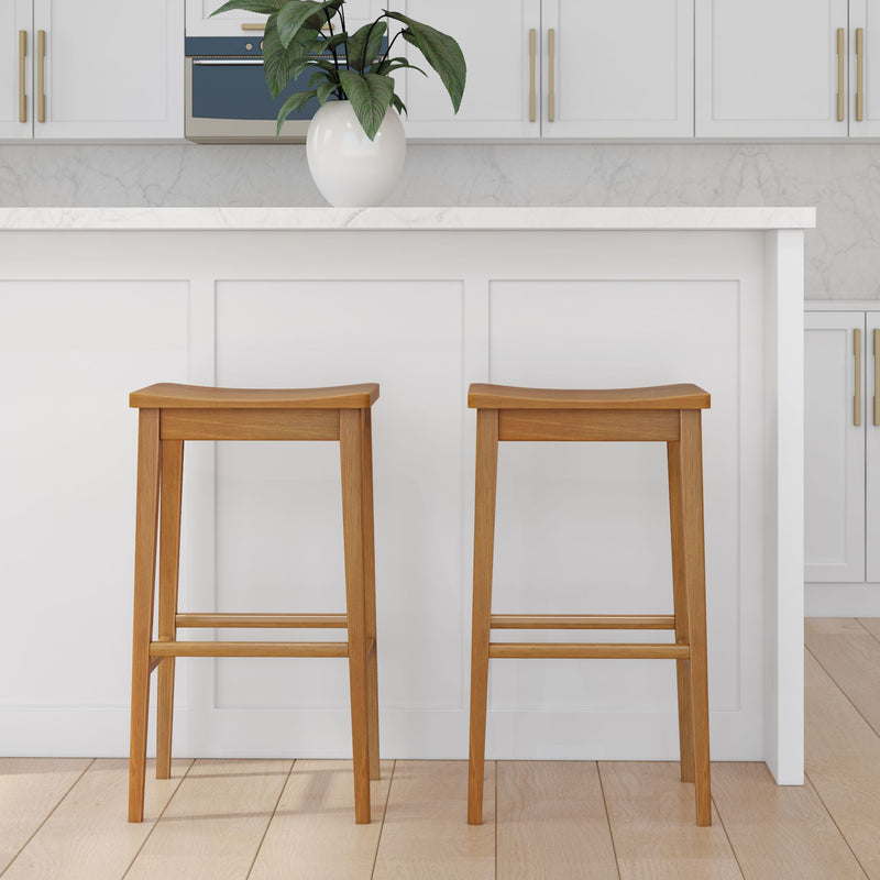 Stylish wooden bar stools in modern kitchen interior with white cabinets and decorative plant.