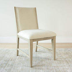 Cream upholstered dining chair with wooden frame on light rug in modern interior.