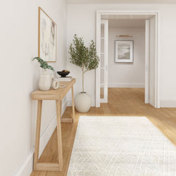 Modern minimalist entryway with light wood console table, neutral wall art, ceramic vases, potted olive tree and hardwood floors