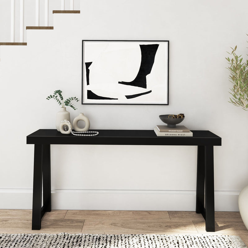 Minimalist hallway with black console table and abstract wall art, featuring decorative vases, stacked books, and wooden flooring.