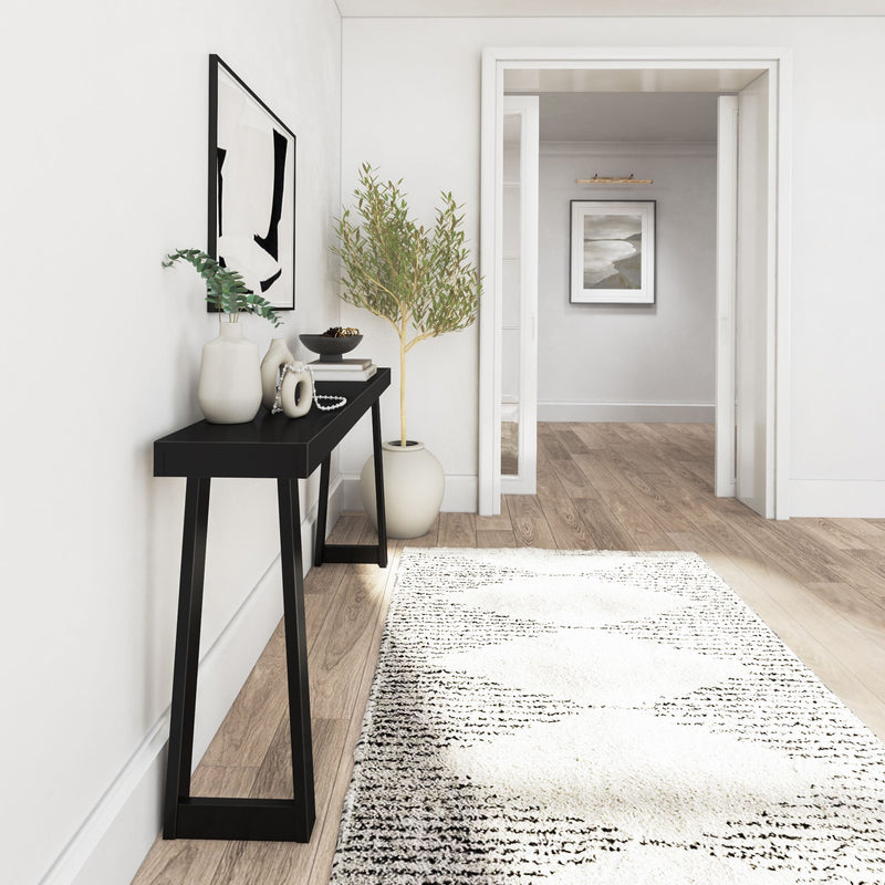 Modern hallway interior design with black console table, decorative vases, and green plant against white walls.