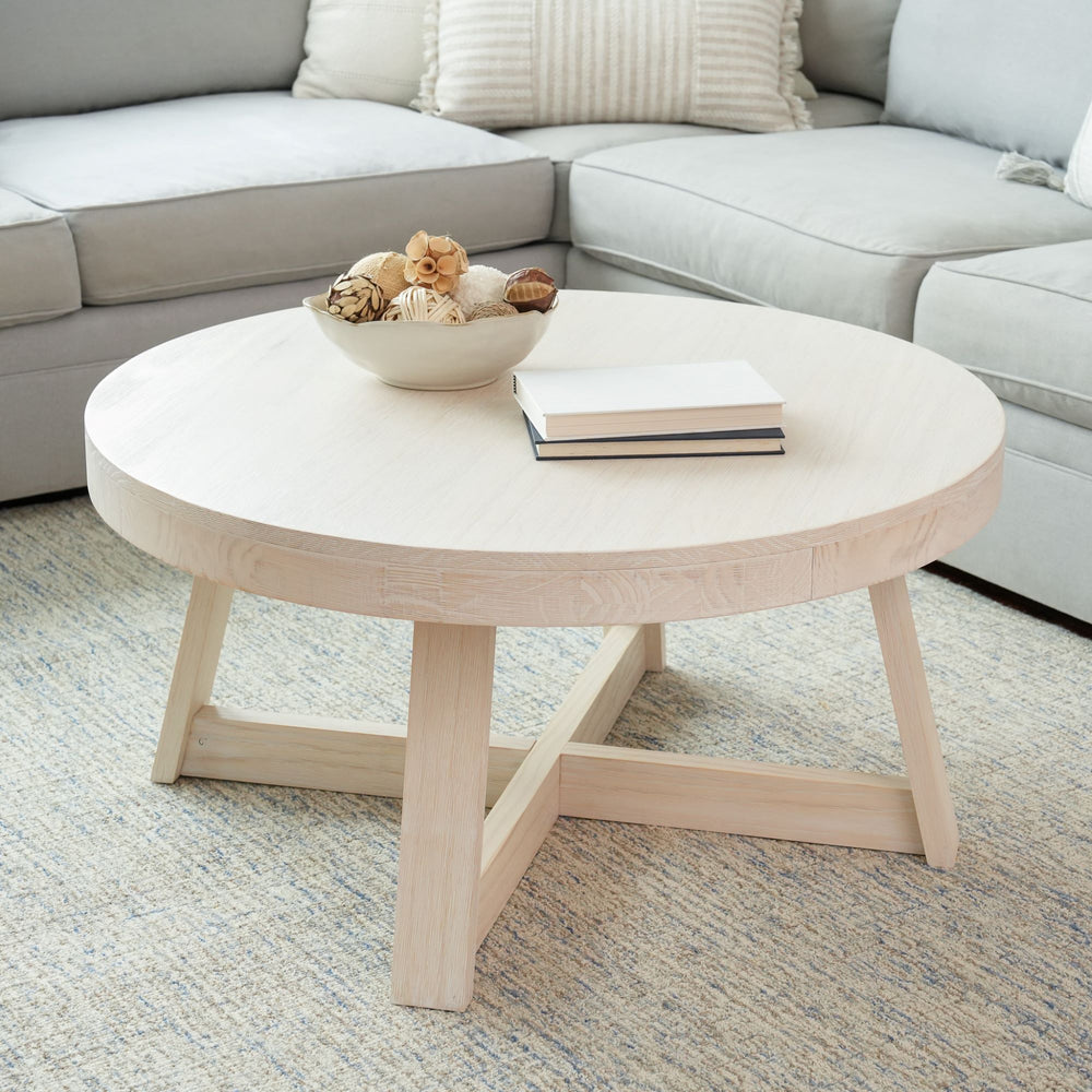 Round wooden coffee table in modern living room with decorative bowl and books.