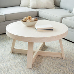 Round wooden coffee table in modern living room with decorative bowl and books.