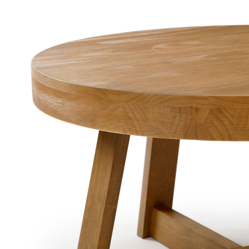 Close-up of round wooden dining table with natural oak finish and angled legs, modern farmhouse style