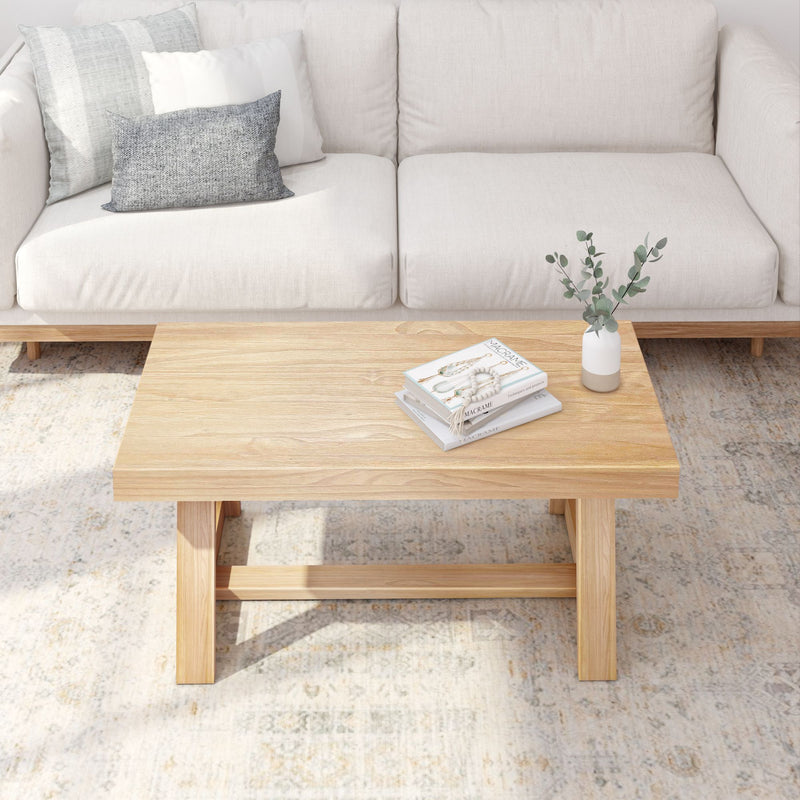 Cozy living room with white sofa, light wood coffee table, decorative books, and vase on a patterned rug.