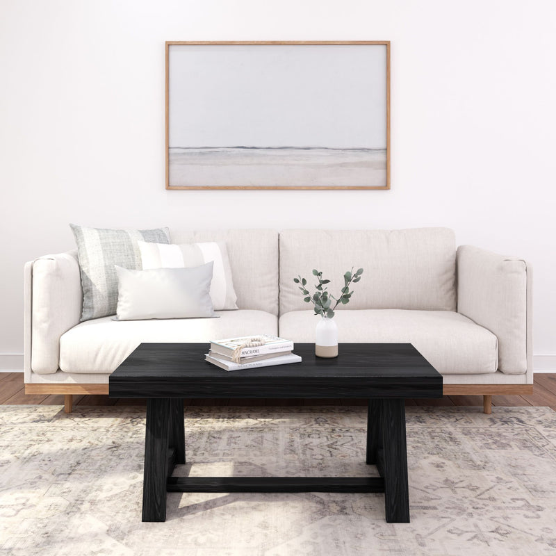 Modern living room with beige sofa, black coffee table, decorative pillows, and minimalist wall art.