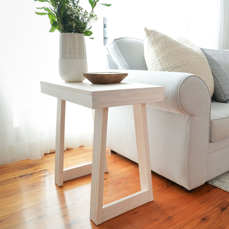 Minimalist white side table with decor, next to a modern beige couch in a bright living room.