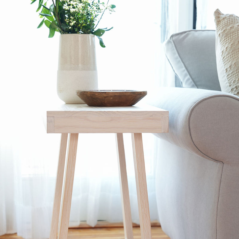 Modern living room with a minimalist wooden side table, decorative vase, and comfortable grey couch.