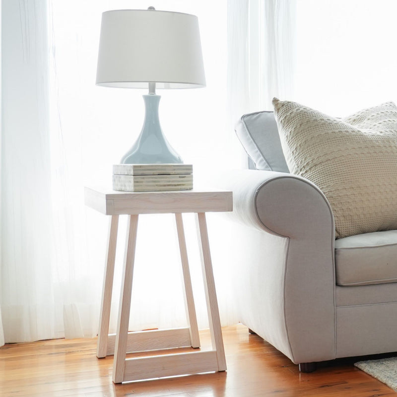 Elegant living room with soft gray couch, textured pillows, and modern wooden side table featuring a stylish ceramic lamp.