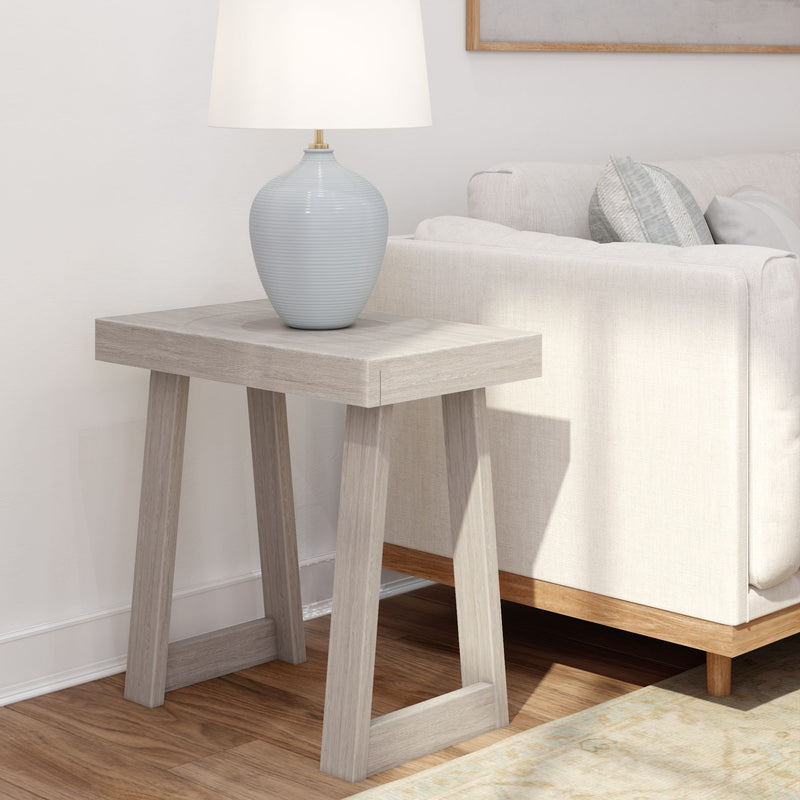 Minimalist wooden side table with a stylish lamp next to a modern beige sofa in a bright living room setting.