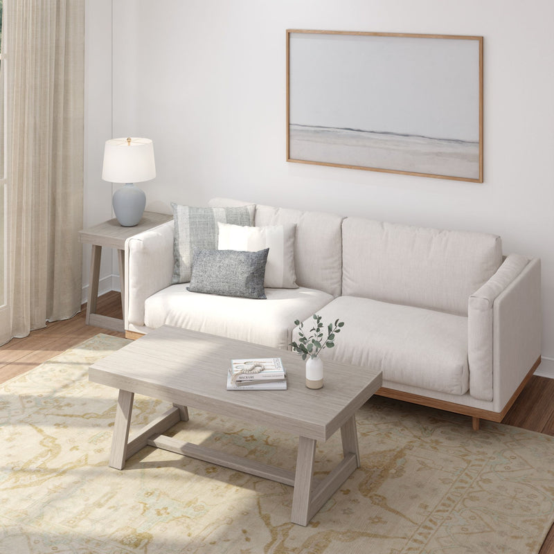 Modern living room with beige sofa, wooden coffee table, minimalist artwork, and decorative cushions.