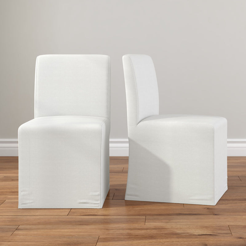 Pair of white slipcovered armless parson dining chairs on hardwood floor, modern minimalist upholstered dining room seating