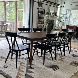 Modern farmhouse dining room with large wooden table and black chairs, textured rug, vase centerpiece and indoor plants, open sliding doors to a screened porch with abundant natural light