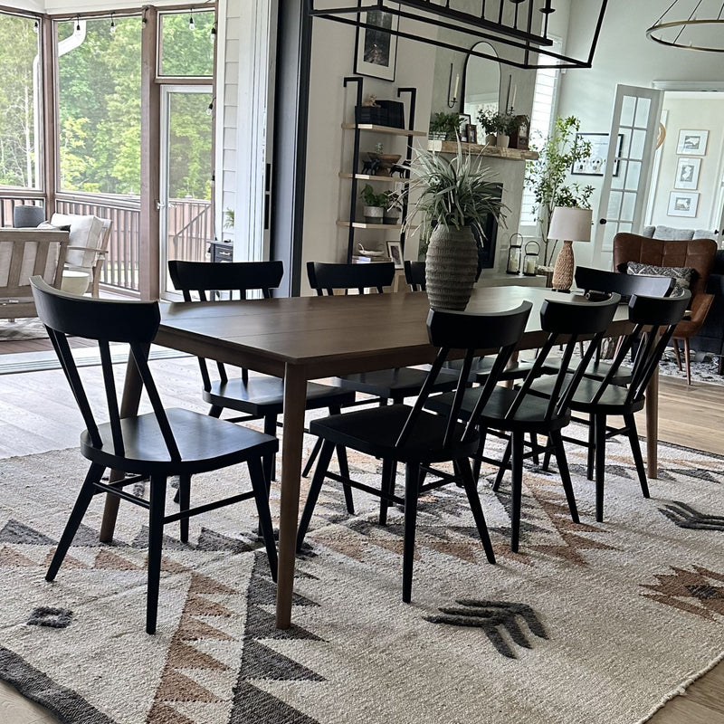 Modern farmhouse dining room with large wooden table and black chairs, textured rug, vase centerpiece and indoor plants, open sliding doors to a screened porch with abundant natural light
