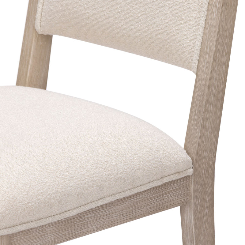 Close-up of a modern beige bouclé upholstered dining chair showing padded seat and back with a light oak wood frame