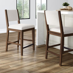 Two modern wooden bar stools with cushioned seats in a bright kitchen setting.