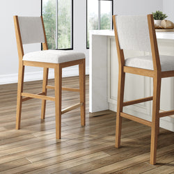 Two modern wooden bar stools with light fabric upholstery in a stylish bright kitchen setting.