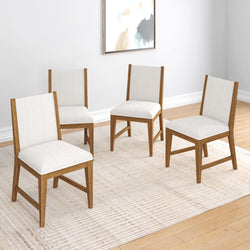 Four modern wooden dining chairs with white cushions on a neutral striped rug in a minimalist room setting.