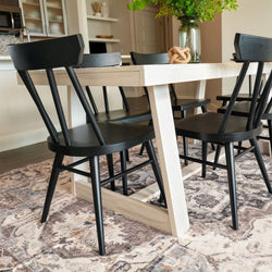 Modern dining room with black chairs and a light wooden table on a decorative rug.