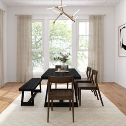 Modern dining room with black wood dining table, wooden chairs and bench, modern pendant light and vase of greenery, large windows with beige curtains, neutral rug and hardwood floors