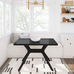 Modern black dining table in a bright kitchen nook with wooden shelves and minimalist decor.