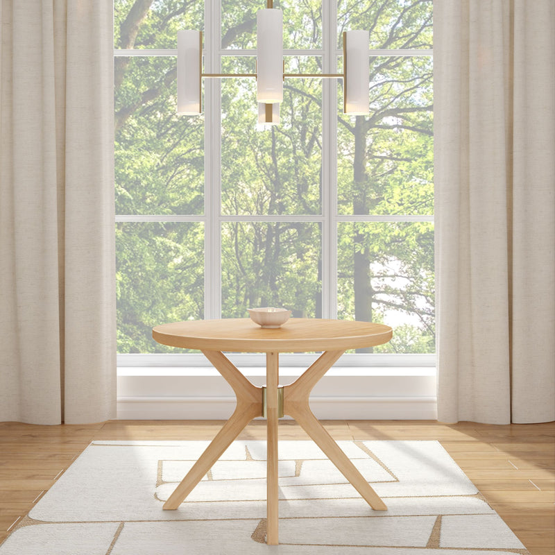 Modern round wooden dining table with contemporary light fixture in bright room with large windows and curtains.