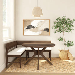Cozy modern dining nook with round walnut table, L-shaped cushioned bench, neutral abstract wall art, woven jute rug, pendant light, and potted ficus in a wicker basket