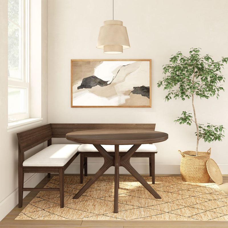 Cozy modern dining nook with round walnut table, L-shaped cushioned bench, neutral abstract wall art, woven jute rug, pendant light, and potted ficus in a wicker basket