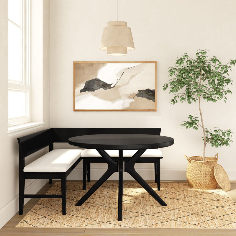 Modern breakfast nook with black round dining table, L-shaped banquette with cream cushions, neutral abstract wall art, pendant light, jute rug and potted ficus in a wicker basket