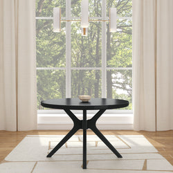 Black round dining table with modern tripod pedestal base in a contemporary dining room, beige curtains, area rug and large window with green forest view
